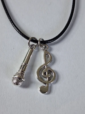Halsband med mikrofon och g-klav/nota  - Vaxat läderhalsband i svart och två silverfärgade berlocker i form av en mikrofon och en g-klav/nota. Perfekt för dig som älskar musik och vill ha en unik accessoar. Materialet rostfritt stål.