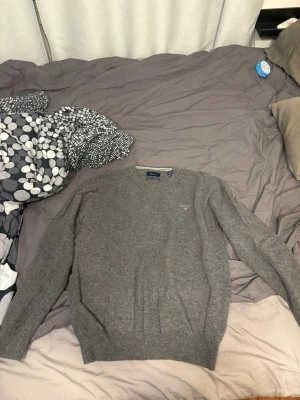 Gant Grå rundhalsad stickad tröja  - Mysig grå stickad tröja med rund halsringning och diskret broderad logga på bröstet. Tröjan har långa ärmar och ribbade muddar vid ärmslut och nederkant. Perfekt för lager på lager under kyliga dagar.