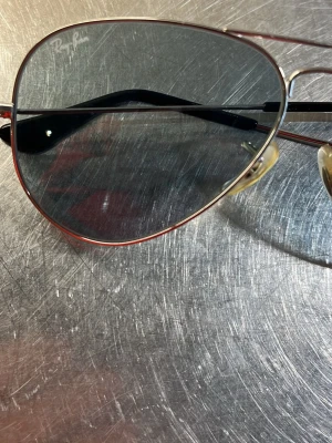 Ray-Ban aviator solglasögon silver - Klassiska Ray-Ban aviator solglasögon med tunna silverfärgade metallbågar och blåa mörktonade  glas. Snygg och tidlös modell som passar till det mesta. Näskuddar i plast för extra komfort och svarta detaljer på skalmarna.