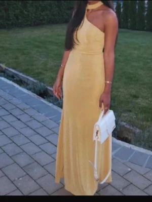 Gul oneshoulder långklänning - Snygg gul långklänning med oneshoulder-design och hög hals. Klänningen har en smickrande passform och ett elegant band som knyts i nacken. Perfekt för dig som vill sticka ut med en unik och trendig look. Kan sänka till 200kr