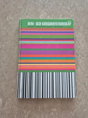 Hem- och konsumentkunskap bok - Kursbok i hem- och konsumentkunskap med hårda pärmar. Omslaget är grönt upptill och har färgglada horisontella ränder i rosa, orange, blått, grönt och svartvitt mönster längst ner. Perfekt för dig som pluggar ämnet och vill ha en tydlig och färgstark bok.