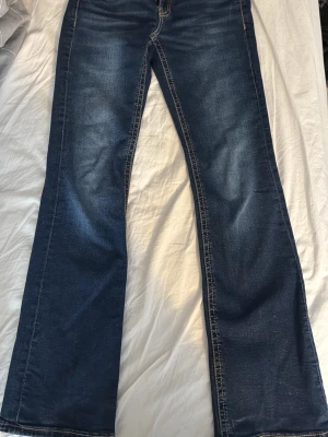 Mörkblå bootcut jeans med nitar - Snygga mörkblå bootcut jeans från Gina tricot. Baktill och på framfickorna finns coola nitar på ena fickan som ger extra edge. Klassisk femficksmodell i stretchigt denimtyg, perfekta till sneakers eller boots. Storlek 164. Nitarna har jag satt dit själv