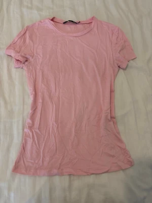 Ljusrosa t-shirt - En enkel och stilren ljusrosa t-shirt från lager 157 i storlek XS. T-shirten har rund halsringning och korta ärmar. Tillverkad i mjuk bomull som känns skön mot huden. Perfekt basplagg att matcha med jeans eller kjol.