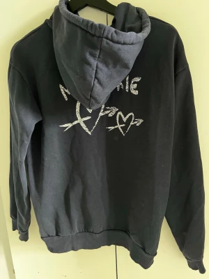 Marinblå hoodie med tryck 'Ma Chérie' - Marinblå hoodie med huva och trycket 'Ma Chérie' i vitt framtill samt ett större tryck med hjärtan och text på ryggen. Mjuk bomullskänsla och ribbade muddar vid ärmslut och nederkant. Perfekt för en avslappnad och cool stil.