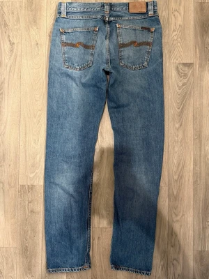 Nudie Jeans Steady Eddie Jeans Blå W31/L34 - Regular Tapered Fit - Nudie Steady Eddie blå jeans i 100% ekologisk bomull, regular tapered fit modell med bekväm passform och klassisk look, storlek W31/L34, midja 40,5 cm, ytterbenslängd 107,5 cm, benöppning 17 cm, modellen är 185cm & väger 65kg, i fint skick.