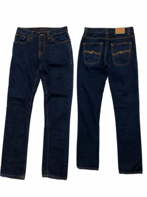Mörkblå jeans från Nudie Jeans - Snygga mörkblå jeans i modellen Grim TimRaka ben och ikonisk broderad detalj på bakfickorna. Perfekta för en stilren och avslappnad look. 31/34