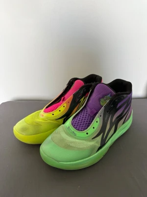  LaMelo Ball Rick and morty Basketskor - Färgstarka Puma MB.01 LaMelo Ball sneakers med gradient i gult, grönt, rosa och lila. Skorna har svart flam-liknande mönster på sidorna, mesh-överdel och broderade detaljer. Mellanhög modell med unik design och textdetaljer på hälen. Perfekta för dig som vill sticka ut på basketplanen. Skick 7,5/10. Kom privat för mer info!