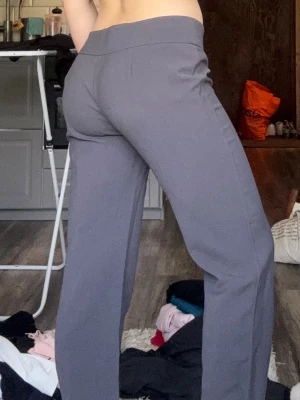 Grå kostymbyxor med bootcut - Snygga grå kostymbyxor med bootcut och hög midja. Byxorna har två knappar framtill och är sydda i ett mjukt, stretchigt material som ger en skön passform. Perfekta för dig som gillar en clean och stilren look.