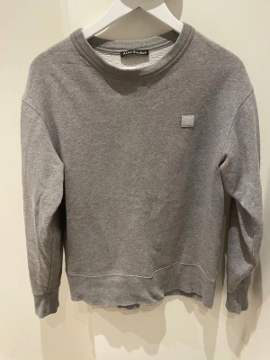 Grå sweatshirt från Acne Studios - Klassisk grå sweatshirt från Acne Studios med rund halsringning och diskret logopatch på bröstet. Tröjan har ribbade muddar vid ärmslut och nederkant. Perfekt för en avslappnad och stilren look.