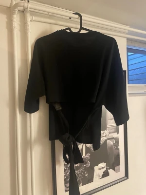 Svart topp med knyt från Nelly - Snygg svart topp från Nelly med knytband bak och rund halsringning. 