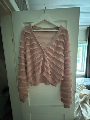Rosa stickad kofta med volangdetaljer - Superfin rosa stickad kofta med volangdetaljer över hela tröjan. Koftan har v-ringning, knappar framtill och långa ärmar. Aldrig använd 💕