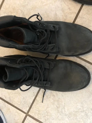 Svarta kängor i skinn med snörning - Säljer ett par svarta kängor i skinn med klassisk snörning och robust design. Perfekta för dig som gillar en tuff och stilren look. Kängorna har högt skaft och grov sula som ger bra grepp. Äkta märke kostade 800kr som ny.