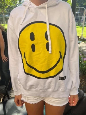 Vit hoodie med smileytryck från Smiley - Vit hoodie med stor gul smiley på framsidan och sex mindre smileys på ryggen. Från Zara. 