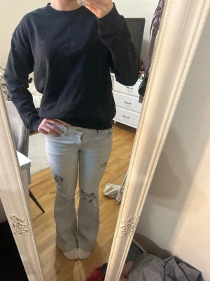 Ljusblå bootcut jeans med slitningar - Säljer ett par ljusblå bootcut jeans med slitna detaljer på knäna och låren. 
