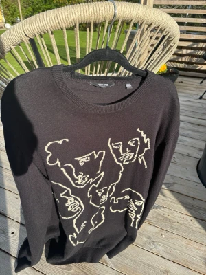 Svart tröja med ansiktsmotiv från ONLY AND SONS - Cool svart tröja från H&M med unikt vitt ansiktsmotiv framtill. Tröjan har rund halsringning och är gjord i mjukt material, perfekt för en avslappnad och trendig look.