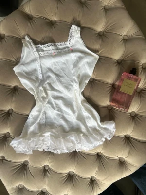 Vitt 2000s linne - Supersöt vit topp med spets längs kanterna och volang nertill. Toppen har smala axelband och små rosa rosetter framtill. Perfekt för en romantisk och feminin look. Materialet känns lätt och luftigt. Finns ej någon etikett så står varken märke eller strl men skulle gissa på XXS🫰