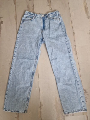 Ljusblå raka jeans i klassisk modell - Säljer ett par ljusblå jeans med rak passform och hög midja. Jeansen har fem fickor, gylf med dragkedja och knapp samt klassiska sömmar. Perfekta för en avslappnad och trendig look.
