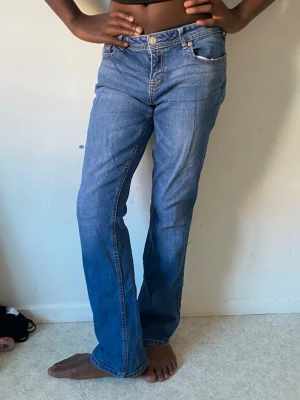 Blå utsvängda jeans med klassisk passform - Säljer ett par blå jeans med utsvängd passform och klassisk femficksdesign. Jeansen har normalhög midja och snygga detaljer på bakfickorna. Perfekta för en avslappnad och stilren look.