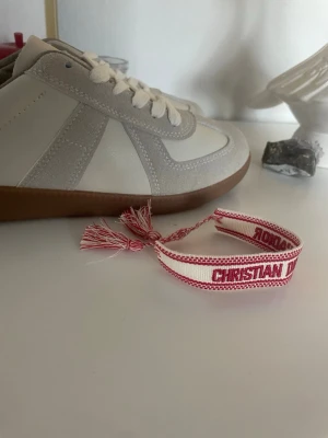 Christian Dior J'Adior armband röd/vit - Snyggt armband från Christian Dior i rött och vitt tyg med texten 'J'Adior'. Justerbar knytning med tofsar i ändarna. Perfekt accessoar för att lyfta din outfit med en exklusiv touch och trendig design.