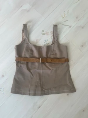 Beige linnetopp med bälte från Zara - Stilren beige linnetopp från Zara med breda axelband och markerad midja tack vare ett snyggt brunt bälte. Toppen har synliga sömmar och är perfekt för en trendig och clean look.