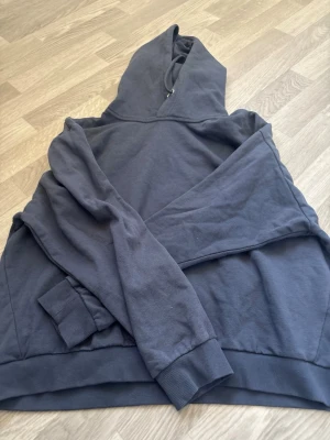 Mörkgrå hoodie med huva - Säljer en stilren mörkgrå hoodie med huva och dragsko. Hoodien har långa ärmar, ribbade muddar och en klassisk känguruficka framtill. Perfekt för en avslappnad look och tillverkad i mjukt bomullstyg.