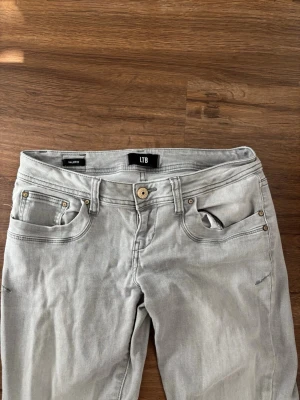 Ljusgrå jeans från LTB - Snygga ljusgrå jeans från LTB med klassisk femficksmodell och raka ben. Jeansen har silverfärgade nitar och en knapp i midjan. Materialet är mjukt och stretchigt för extra komfort. Perfekta till en avslappnad stil.