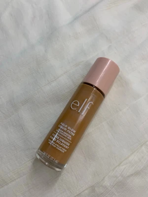 e.l.f. Halo Glow Liquid Filter Medium/Tan - e.l.f. Halo Glow Liquid Filter i nyansen Medium/Tan (Shade 5). Flytande foundation i glasflaska med rosa lock, ger en glowig finish och jämnar ut hudtonen. Perfekt för dig som vill ha en naturlig lyster och medium täckning.