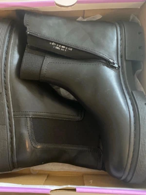 Svarta Chelsea boots med dragkedja - Stilrena svarta Chelsea boots i slätt läder med resår på sidorna och dragkedja på insidan. Klassisk rund tå och robust sula ger en cool look. Perfekta för dig som vill ha en tidlös och trendig sko till hösten och vintern.