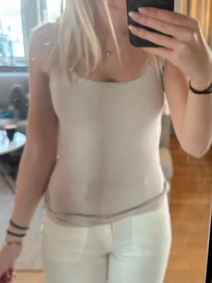 Beige ribbad linnetopp - Snygg beige linnetopp med rund halsringning och ärmlös design. Toppen är ribbad och sitter tight mot kroppen, perfekt att styla med jeans eller kjol. Enkel och stilren look som passar till många outfits.