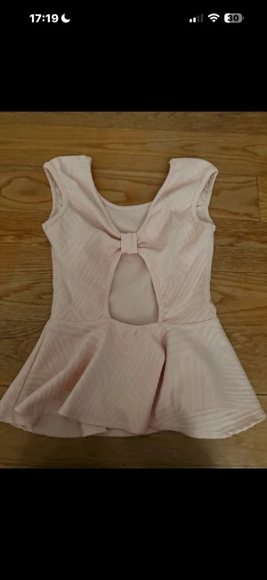 Ljusrosa peplumtop med rosett - Söt ljusrosa peplumtop med subtilt mönster och rund halsringning. Toppen har ärmlös design, en rosett och en öppen detalj i ryggen. 