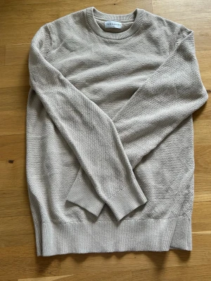 Beige stickad tröja These Glory Days - Säljer en stilren beige stickad tröja från These Glory Days. Tröjan har rund halsringning, ribbade muddar och en diskret strukturstickning som ger en snygg textur. Perfekt till jeans eller chinos för en clean look.