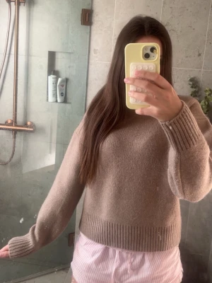 Beige stickad tröja från Primark - Mysig beige stickad tröja från Primark med rund halsringning och breda ribbade muddar vid ärmslut och nederkant. Tröjan har en rak passform och är tillverkad i ett mjukt material som känns lyxigt och skönt.