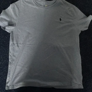 Grå t-shirt från Polo Ralph Lauren - Snygg grå t-shirt från Polo Ralph Lauren med klassisk rund hals och korta ärmar. Diskret Polo-logga broderad på bröstet. Mjuk och skön bomull som passar perfekt till jeans eller shorts. Enkel och stilren design som alltid funkar.