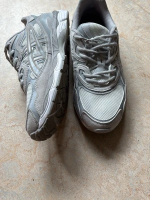 Gråa Asics sneakers mesh och syntet - Snygga grå/krämfärgade sneakers från Asics med klassiska ränder på sidan i ny skick och endast använd 2-3 gånger. Perfekta för sportsammanhang eller till vardagen. (Ny pris 1800kr)