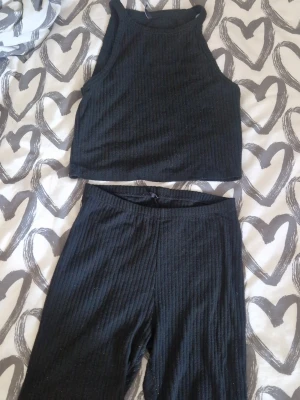 Ribbat set - Säljer ett svart ribbat set med matchande crop top och höga shorts. Toppen har hög hals, medan byxorna är tajta och midjehöga. Materialet är stretchigt och mjukt, perfekt för en trendig och bekväm look. Noppriga!