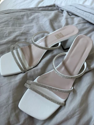 Vita sandaler  - Stilrena vita sandaler med fyrkantig tå och tre tunna remmar täckta av glittrande strass. De är helt oanvända endast testade. Perfekta för att lyfta vilken outfit som helst.