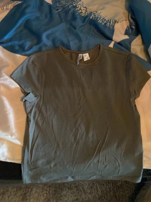 Mörkgrön basic t-shirt - En enkel mörkgrön t-shirt med rund hals och korta ärmar. Tillverkad i mjuk bomull, perfekt för en avslappnad och stilren look. Passar till det mesta och är ett måste i garderoben.