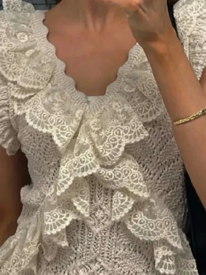 Stickad topp med spetsvolanger - En gullig cremevitt/beige stickad topp med V-ringning. Toppen har väldigt fina volanger samt detaljer och ett  underbart mönster. Den passar perfekt nu till sommaren. Den är både trendig och modern. Toppen är i storlek S.( Första och sista bilden visar hur den sitter på och den tredje bilden är min)