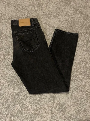 Svarta jeans från Tiger of Sweden - Säljer ett par svarta jeans från Tiger of Sweden med klassisk femficksdesign och raka ben. Jeansen har en snygg mörk tvätt och är tillverkade i bomull. Perfekt för dig som gillar stilrena och tidlösa plagg. Storlek 28/30.