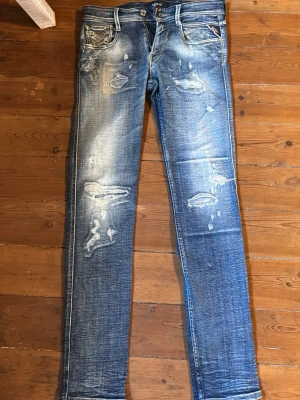 Blå slitna skinny jeans från Replay - Säljer ett par blå skinny jeans från Replay med slitningar och distressed detaljer framtill. Jeansen har klassisk femficksmodell, dragkedja i gylfen. Materialet är denim i bomull med stretch för extra komfort.