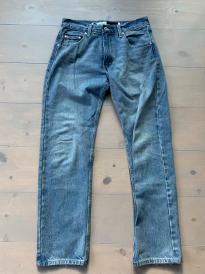 Blå raka jeans från Levi's 501 - Klassiska blå jeans från Levi's med rak passform och fem fickor. Jeansen har en snygg tvättad look och är tillverkade i slitstark denim. Perfekta för en avslappnad stil och funkar till det mesta. Levi's-logga på bakfickan.