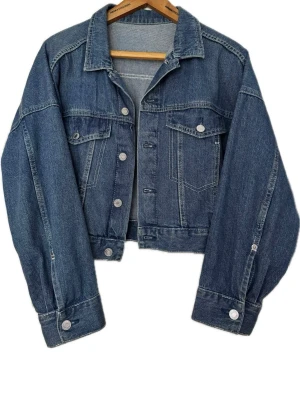 Blå croppad jeansjacka - Snygg croppad jeansjacka i klassisk blå denim med knappar framtill och två bröstfickor. Köpt på H&M tror jag! 