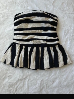 Randig axelbandslös tubtopp - Snygg svartvit randig tubtopp med volang nedtill. Toppen är axelbandslös och har en peplum-liknande form som ger en cool och trendig siluett. Perfekt att styla med jeans eller kjol för en statement-look. Har prislapp kvar säljer då den var för stor. 