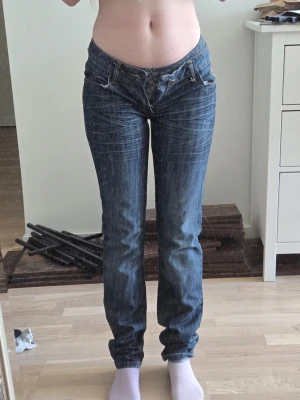 Blå low waist jeans Playboy - Säljer ett par blå low waist jeans med raka ben och snygga slitningar. Jeansen har en guldfärgad broderad playboy logo vid fickan och dekorativt mönster på insidan av linningen samt mycket playboy kaniner runt om midjan.. Klassisk femficksmodell i denim. För små för mig tyvärr.. 