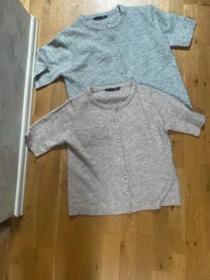 Två stickade koftor med pärlknappar - Två mysiga stickade koftor i ljusgrått och beige, båda med rund halsringning och pärlknappar framtill. Koftorna har halvlånga ärmar och en avslappnad passform, perfekta att slänga på sig över en t-shirt. Materialet ser mjukt och fluffigt ut.                                PRIS KAN DISKUTERAS‼️