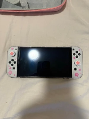 Nintendo Switch OLED - Säljer min Nintendo Switch OLED i nästintill nyskick. Konsolen köptes i februari från maxgaming och har använts väldigt sparsamt, då den mestadels har legat skyddad i sitt fodral.  Det ingår 3 spel samt alla originaltillbehör som följde med vid köpet, flera extra tillbehör som jag köpt till i efterhand.  Konsolen har haft både skärmskydd och fodral från dag ett, vilket gör att den är mycket välbevarad utan synligt slitage. Jag skulle själv beskriva skicket som nyskick. Paket pris : 4000kr