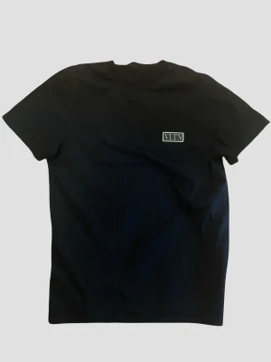 Svart VLTN t-shirt från Valentino - Snygg svart t-shirt från Valentino med VLTN-logga på bröstet. Klassisk passform och rund halsringning. Tillverkad i mjuk bomull som känns skön mot huden. Perfekt för dig som gillar stilrena och exklusiva plagg. XXL (motsvarar snarare L-XL i verkligheten) 