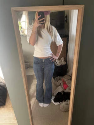 Blå bootcut jeans med fickor - Säljer ett par blå bootcut jeans med hög midja och stora fickor fram. Jeansen har en klassisk blå tvätt och stängs med dragkedja och knapp. Perfekta för en avslappnad och trendig look.