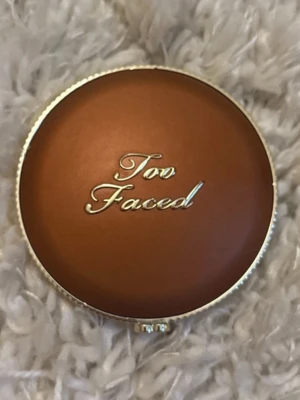 Too Faced Milk Chocolate Soleil Bronzer - Säljer en Too Faced Milk Chocolate Soleil bronzer i en rund, brun och guldig dosa med elegant logga på locket. Pudret ger en naturlig solkysst look och har en matt finish. Perfekt för att skulptera ansiktet eller ge extra glow.