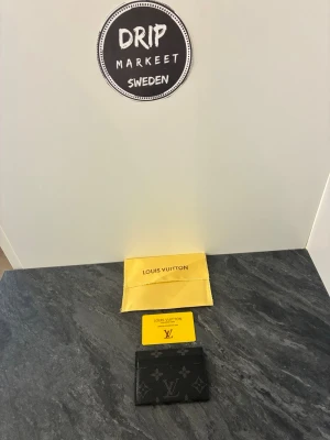  svart monogram korthållare - Snygg svart korthållare med klassiskt monogrammönster i grått. Tillverkad i exklusivt läder och levereras med original gul påse och äkthetskort. Perfekt för dig som vill ha en stilren och lyxig accessoar till dina kort.